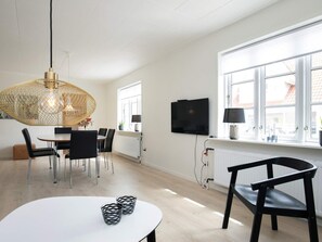 Una sala de estar moderna con comedor, televisor montado en la pared y un gran ventanal que proporciona luz natural.
