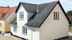 A white two-story house with a steeply pitched roof, a small porch, and a visible front door. - 4 Star Holiday Home in Lokken (Lokken)