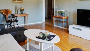 A living room with a sofa, a coffee table, a TV, a wooden side table with a vase, and a painting on the wall. - 6 Person Holiday Home in Visby-by Traum (Visby)