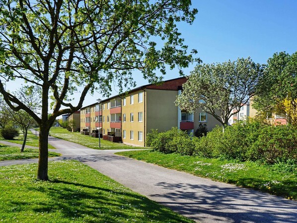 Un immeuble résidentiel doté de nombreux balcons, d’un chemin pavé et entouré de verdure.