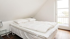 A bedroom with a bed, a nightstand, a lamp, and a window. - 4 Star Holiday Home in Skagen (Skagen)