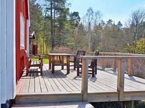 A wooden deck with a red building, outdoor seating, and a forested backdrop.
