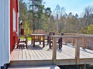 A wooden deck with a table and chairs, a red building, and a forested background. - 6 Person Holiday Home in Vaxholm (Vaxholm)