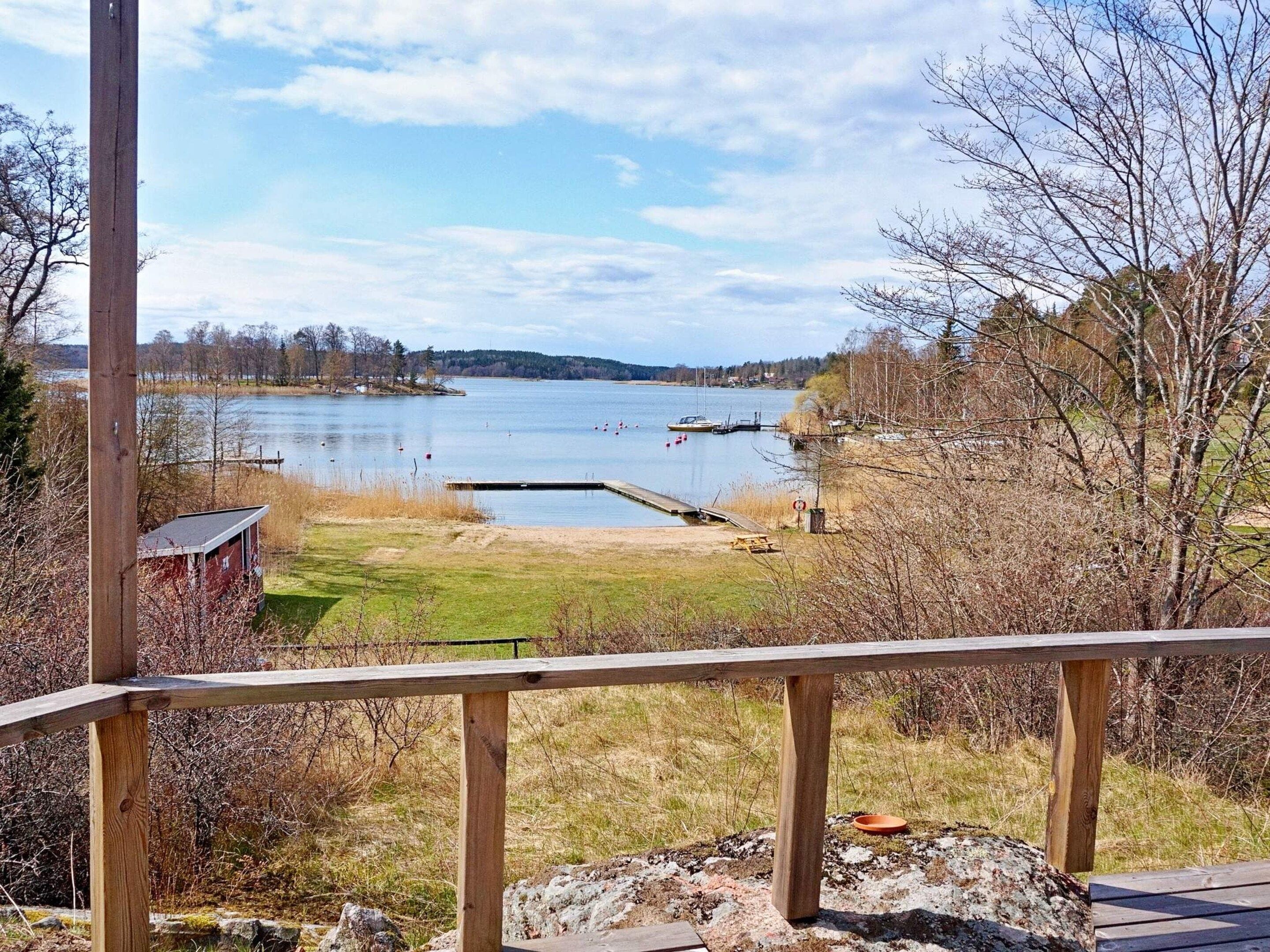Une vue sur le lac depuis une terrasse en bois, avec un quai s’avançant dans l’eau, le tout entouré d’arbres et d’une zone herbeuse.
