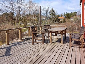 A wooden deck with a table and chairs, surrounded by trees and a building in the background.