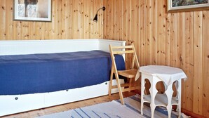 A room with a wooden paneled wall, a bed with a blue bedspread, a wooden chair, a small white table, and two framed pictures. - 6 Person Holiday Home in Vaxholm (Vaxholm)