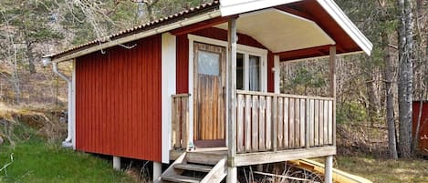 Una cabaña pequeña con un porche, escalones de madera y una puerta.