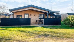 Ein modernes, zweistöckiges Haus mit Holzfassade, schwarzem Dach und einem eingezäunten Garten.