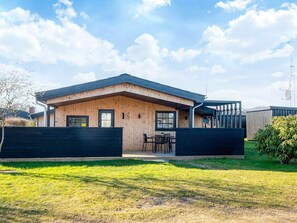 Une maison moderne à deux étages, avec une façade en bois, un toit noir et une cour arrière clôturée.