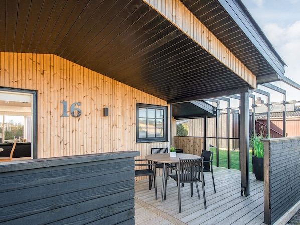 A wooden deck with a table and chairs, a window, and a number '16' on the wall.