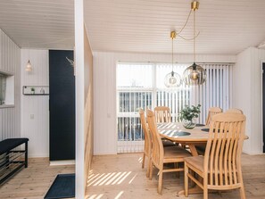 A dining area with a wooden table and chairs, a black bench, and a window with blinds.