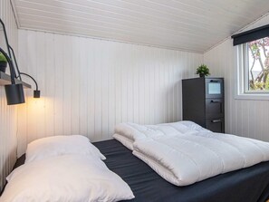A room with two beds, a desk, a cabinet, and a window with a view of trees.