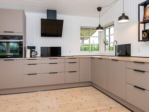 A modern kitchen with wooden flooring, built-in appliances, and a large window providing natural light.