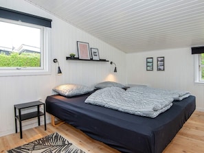 A bedroom with a bed, a small table, a shelf with pictures, and a window.