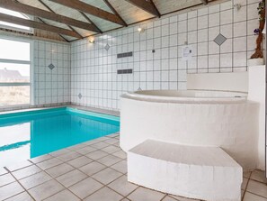 Une piscine avec un revêtement intérieur en carrelage, un jacuzzi et une fenêtre offrant une vue agréable.