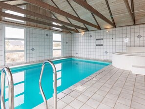 Une piscine intérieure à l’eau d’un bleu limpide, avec des murs carrelés et une structure de plafond en bois.