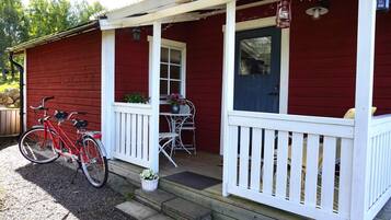 A red wooden house with a white porch, a blue door, and a bicycle parked outside.