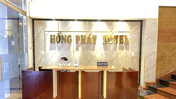 Tauleller de recepció a l'Hotel Hong Pat amb un fons de paret de marbre i un cartell que indica vendes i servei de visats i passaport.
