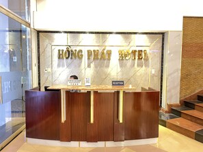 A reception desk at Hong Pat Hotel with a marble wall backdrop and a sign indicating sales and a visa passport service. - HONG PHAT HOTEL (Ho Chi Minh City)