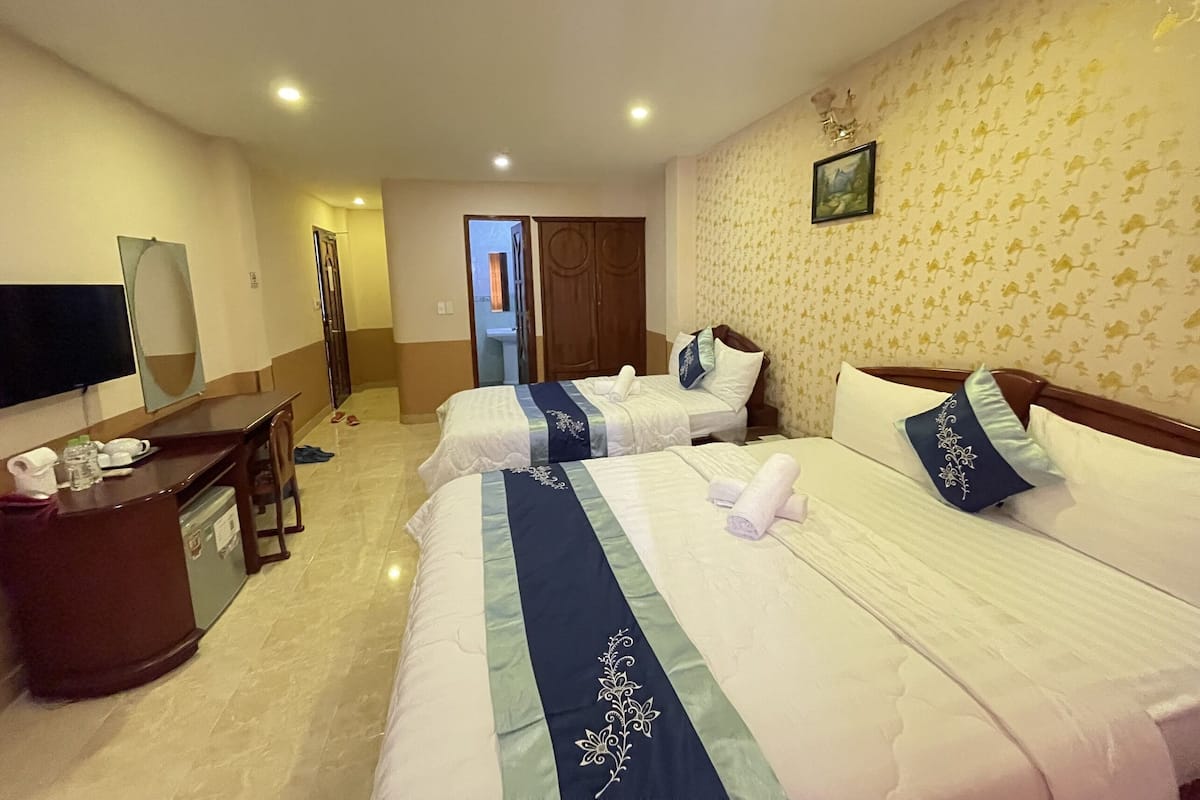 Habitación de hotel con dos camas, un escritorio, un televisor y un baño visible a través de una puerta abierta.