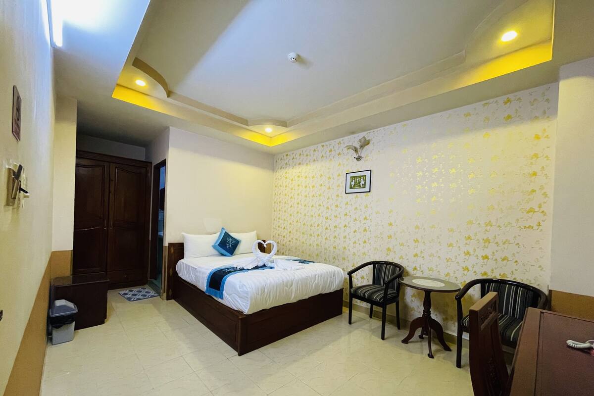 Una habitación de hotel con una cama, dos sillas, una mesita y un armario.
