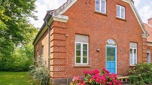 A red brick house with a blue door, surrounded by a well-maintained garden with flowering plants. - 4 Star Holiday Home in Ulfborg (Ulfborg)