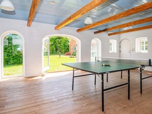 A ping pong table in a room with wooden beams and large arched windows.