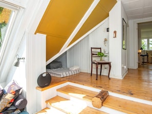 A room with a sloped ceiling, a wooden staircase, a chair with a plant, and a bed with a striped blanket.