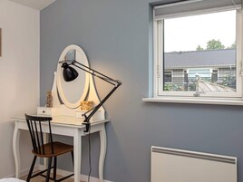 Et værelse med et skrivebord, stol og et vindue med udsigt til et hus.