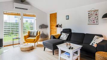A modern living room with a sofa, armchair, and coffee table, a wooden door, and a view through a window.