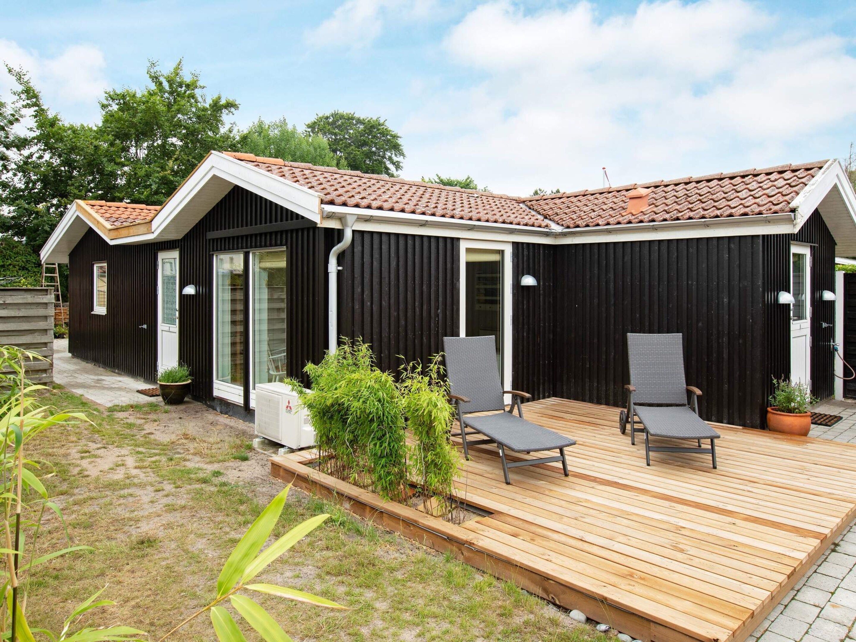 Ein modernes Gebäude mit einer Holzterrasse, zwei Liegestühlen und einem kleinen Garten.