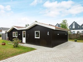 En sort metalbygning med et tag af fliser, en hvid dør og to vinduer.