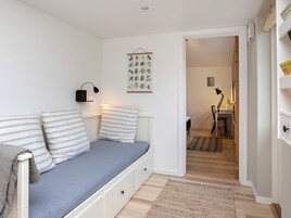 Et værelse med en seng, en sengebordlampe, en vægmonteret lampe og en dør til et andet rum.