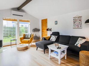 A modern living room with a sofa, armchair, and coffee table, a wooden door, and a view through a window. - 6 Person Holiday Home in Vaeggerlose (Vaeggerlose)