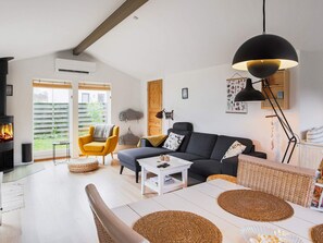 A modern living room with a fireplace, a sofa, a yellow armchair, and a dining area with a table and chairs.