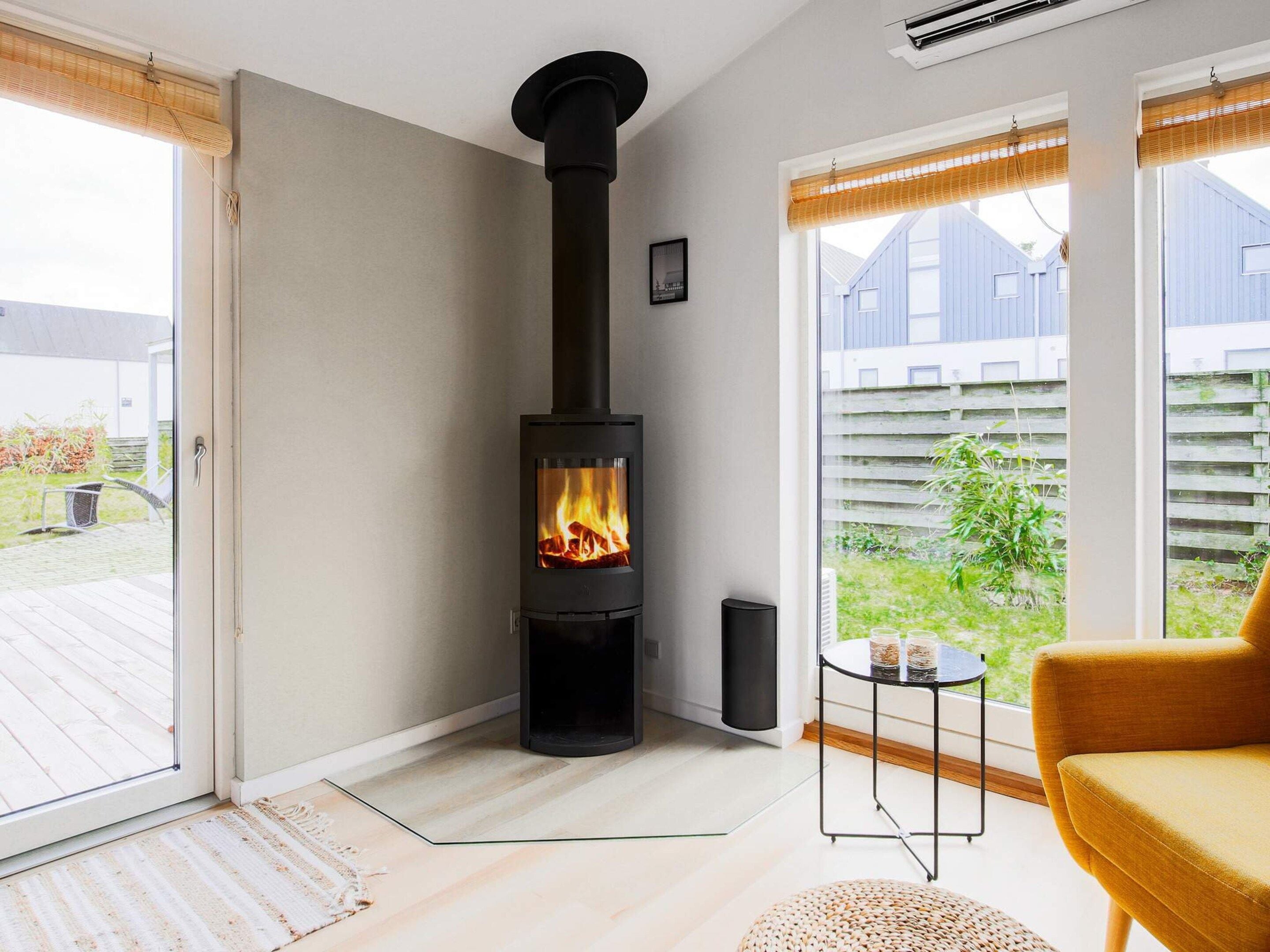A modern interior with a wood-burning stove, a glass door leading outside, and a view of a backyard.