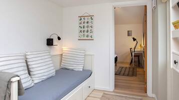 A room with a bed, a bedside lamp, a wall-mounted light, and a door leading to another room.