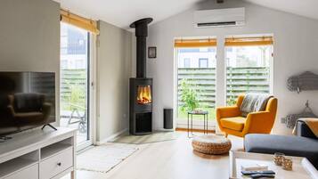 A modern living room with a fireplace, a sofa, a television, and a window with a view of greenery.