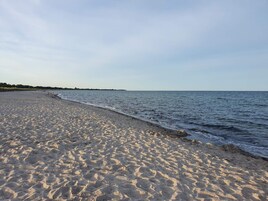 En sandstrand med bløde bølger, en klar himmel og en fjern kystlinje.
