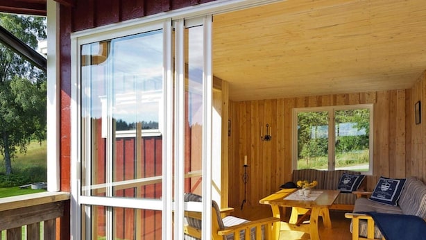 A wooden cabin with a large sliding glass door, a wooden deck, a sofa, a table, and a chair. - 4 Star Holiday Home in Bralanda (Bralanda)