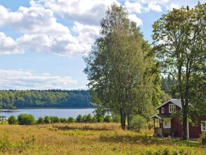 A house with a red exterior and a white trim, situated near a lake with a forested shoreline. - 4 Star Holiday Home in Bralanda (Bralanda)