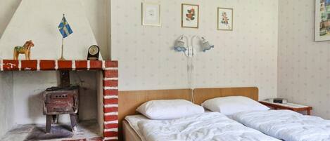 A room with a brick fireplace, a bed with white bedding, and a wall with framed pictures.