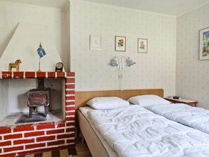 A room with a brick fireplace, a bed with white bedding, and a wall with framed pictures.