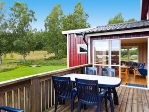 A wooden deck with a table and chairs, a covered seating area with a view of the outdoors, and a red building with a window.