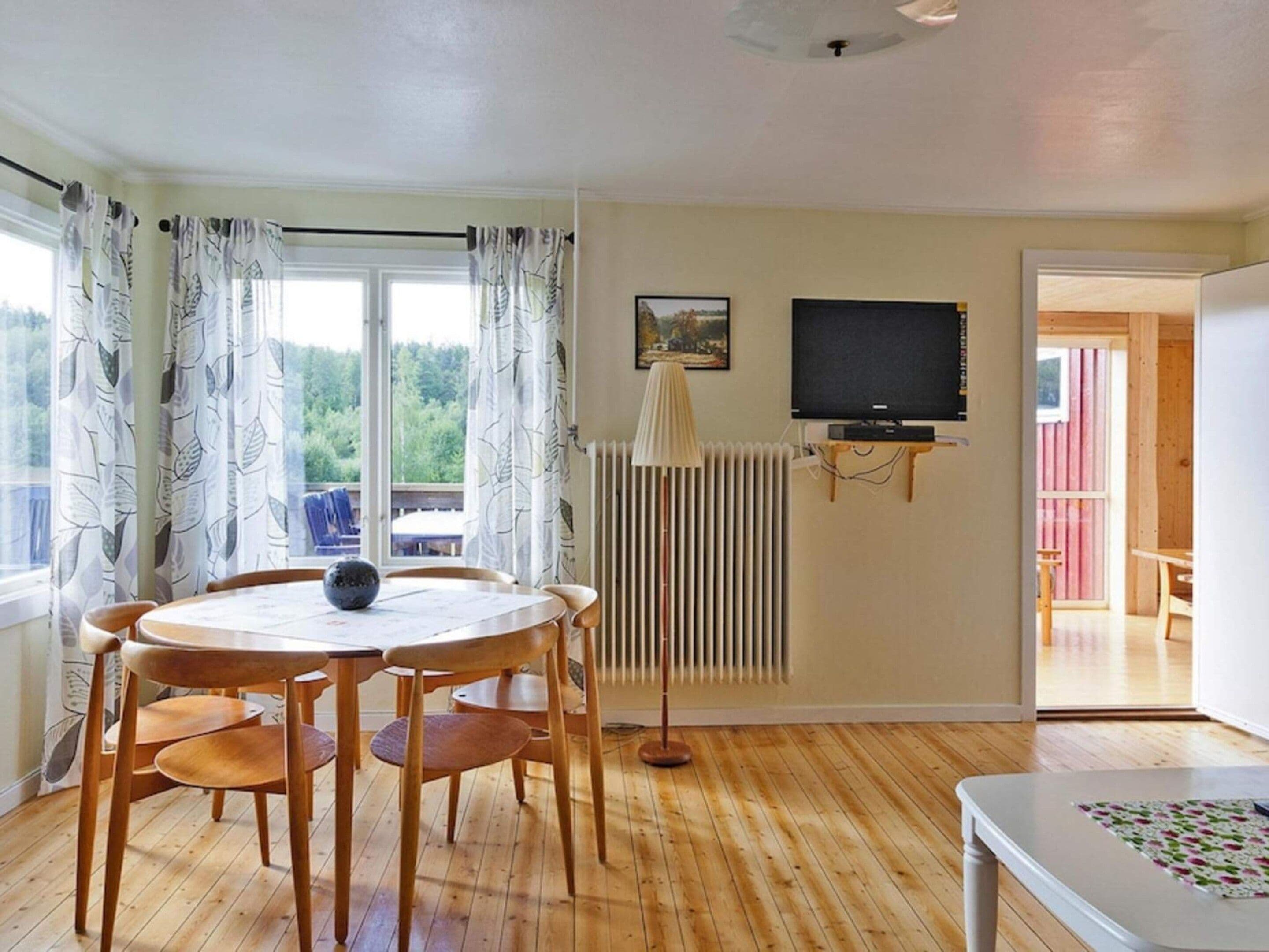 Ein Zimmer mit Esstisch, Stühlen, Heizkörper, Fernseher und Blick ins Freie.
