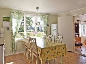 A dining area with a table and chairs, a window with curtains, a refrigerator, and a bookshelf.