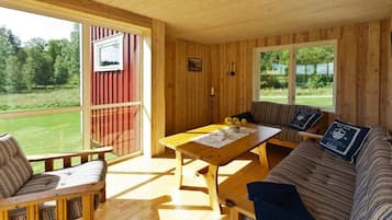 A wooden cabin interior with a sofa, a table, and a bench. There are two windows providing views of the outdoors.