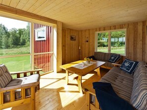 A wooden cabin interior with a sofa, a table, and a bench. There are two windows providing views of the outdoors.