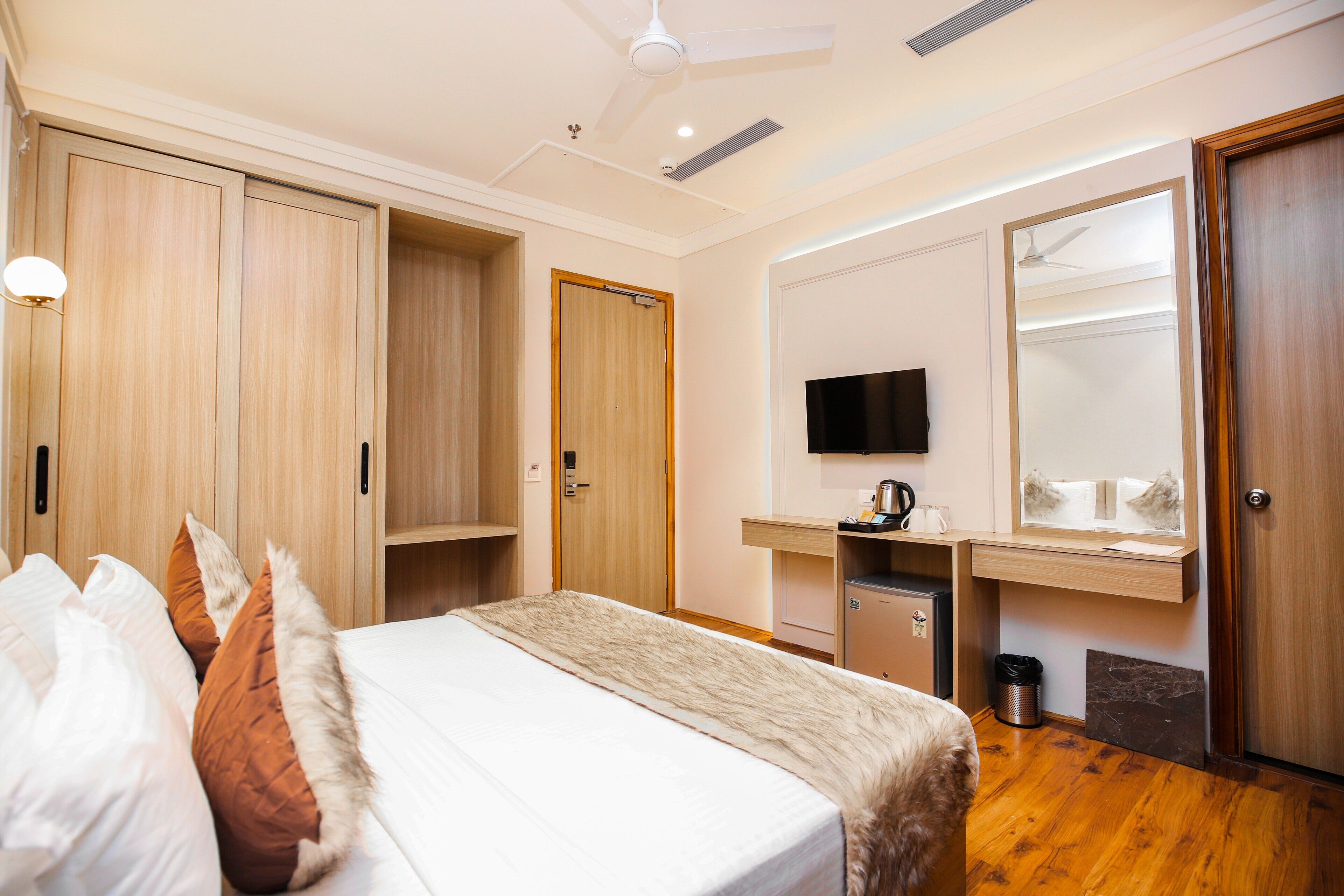 A hotel room with a bed, wardrobe, desk, mirror, TV, and a small kitchenette.