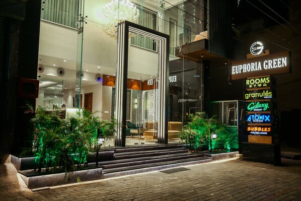 Entrada d'hotel amb façana de vidre, escala que condueix a la llotja i indicadors il·luminats per diferents serveis, incloent habitacions, un banquet i un bar al terrat.